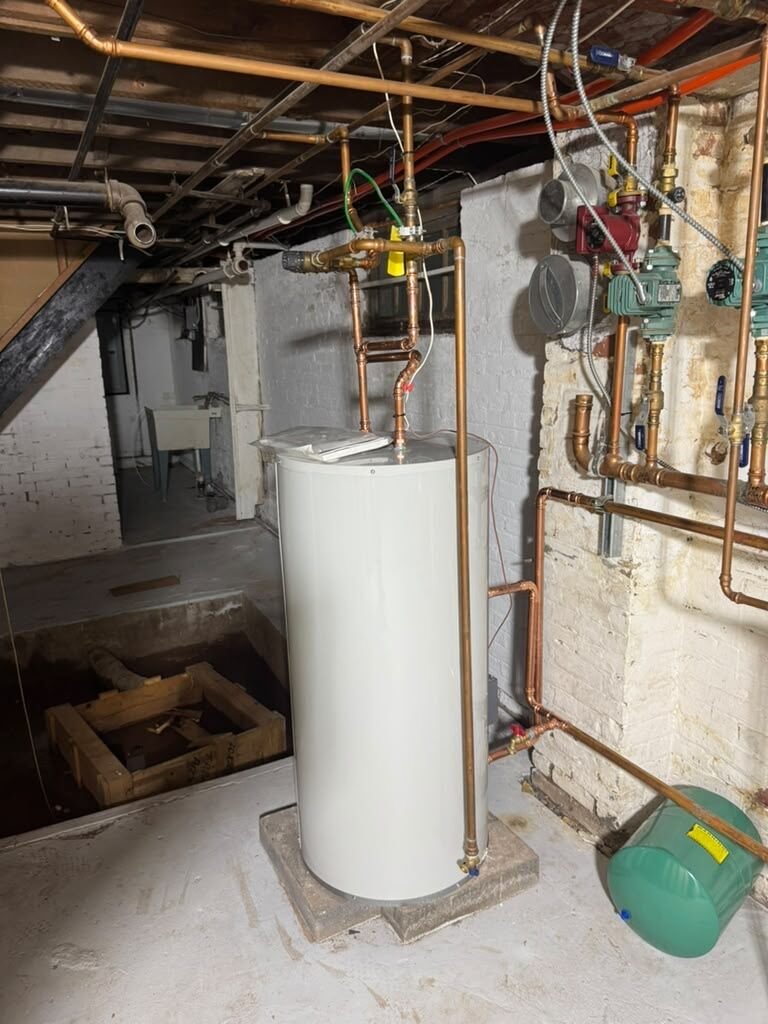 A storage water heater connected to overhead copper boiler piping with circulators and zone controls in a basement