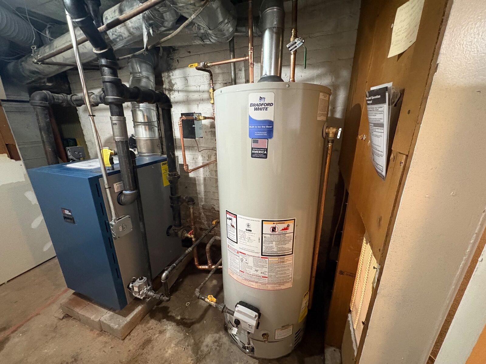 A Bradford White gas water heater installed next to an existing gas boiler in a residential basement.